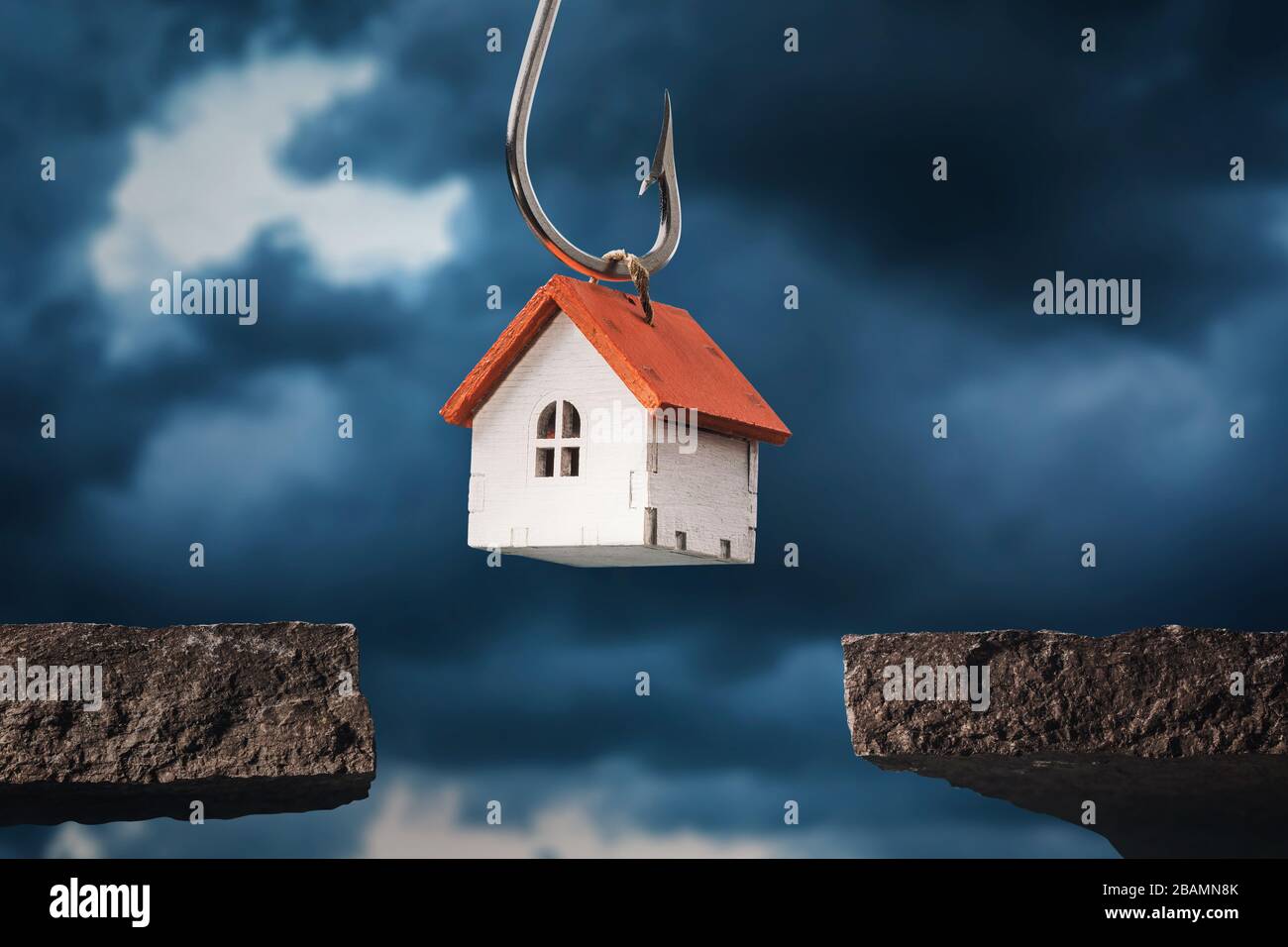 A toy house on a hook hanging over a precipice. Debt concept Stock Photo