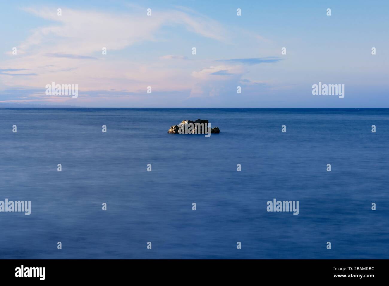 A rock in the middle of the sea. The sky is blue with clouds Stock ...