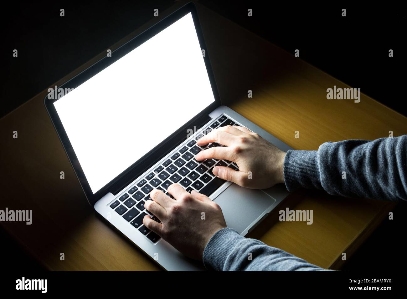 Man working on laptop with white screen glowing in the dark on a wooden ...