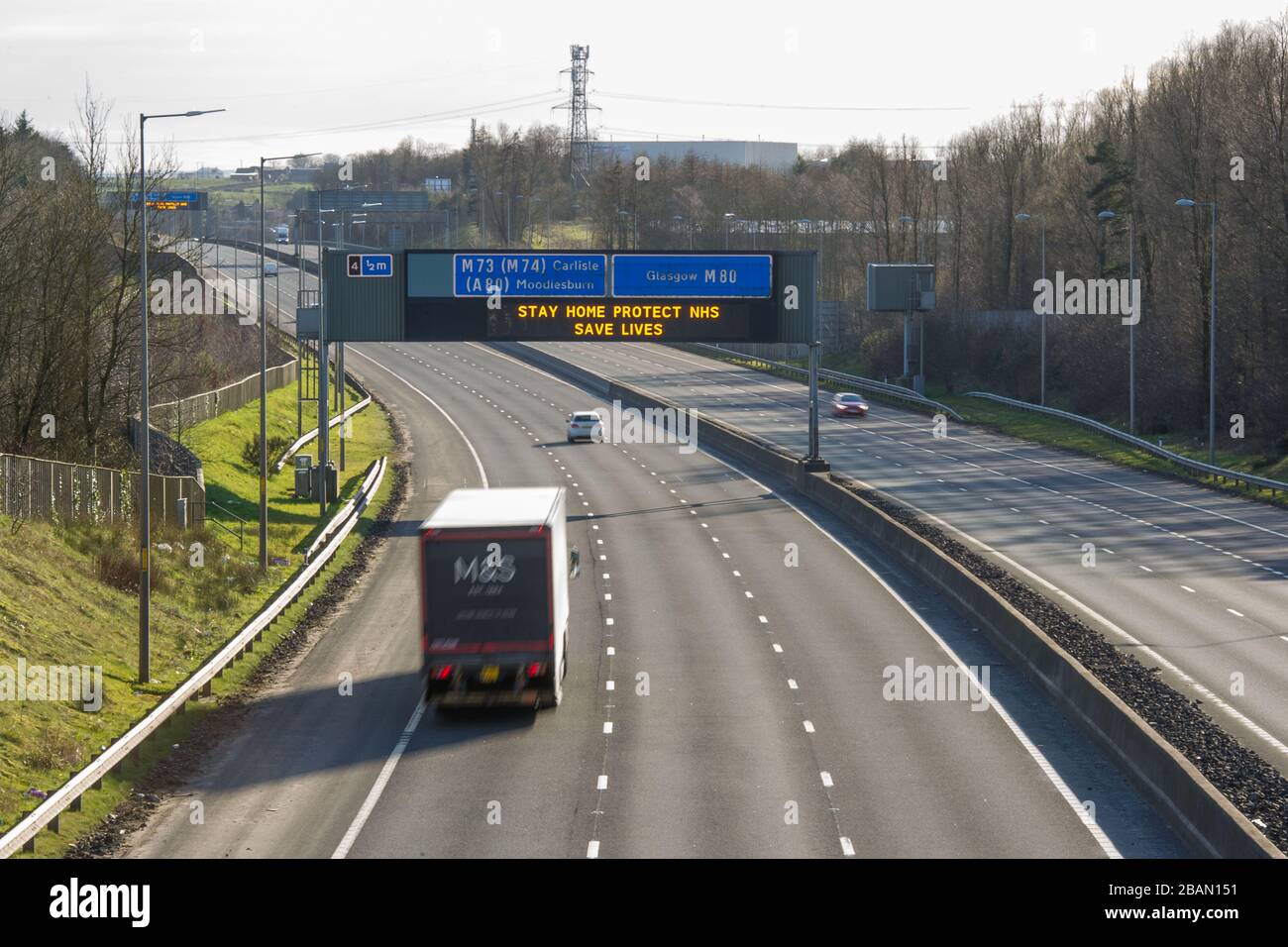 Glasgow, UK. 28th Mar, 2020. Pictured: Road signs all along the M8 and M80 motorways which read, “STAY HOME PROTECT NHS SAVE LIVES” The Coronavirus Pandemic has forced the UK Government to order a shut down of all the UK major cities and make people stay at home, which has left the motorways and all other roads free of the usual nose to tail traffic which would otherwise be there. Credit: Colin Fisher/Alamy Live News Stock Photo