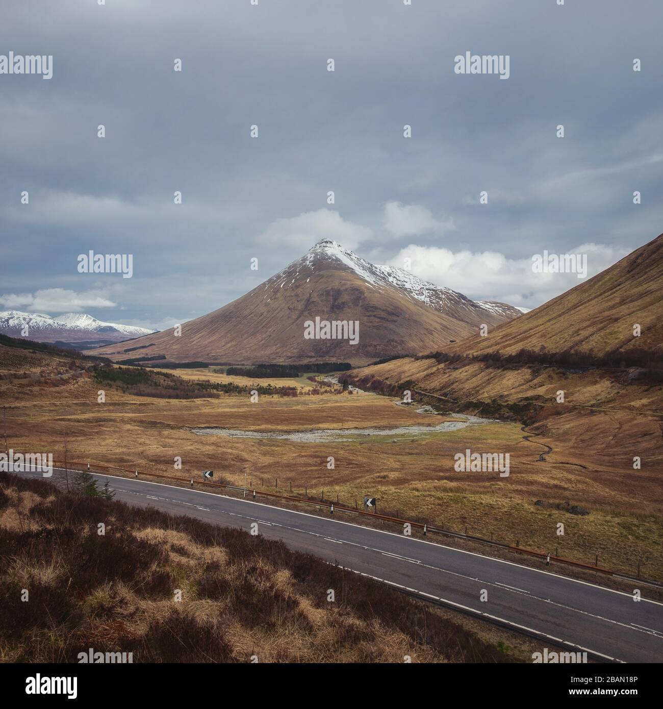 Open road leading through the Scottish Highlands of Glen Coe, snowcapped mountains, and river valley Stock Photo