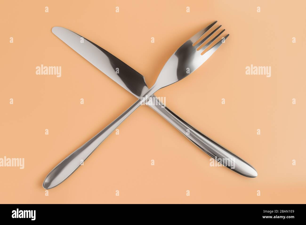 Crossed fork and knife on beige table top view Stock Photo
