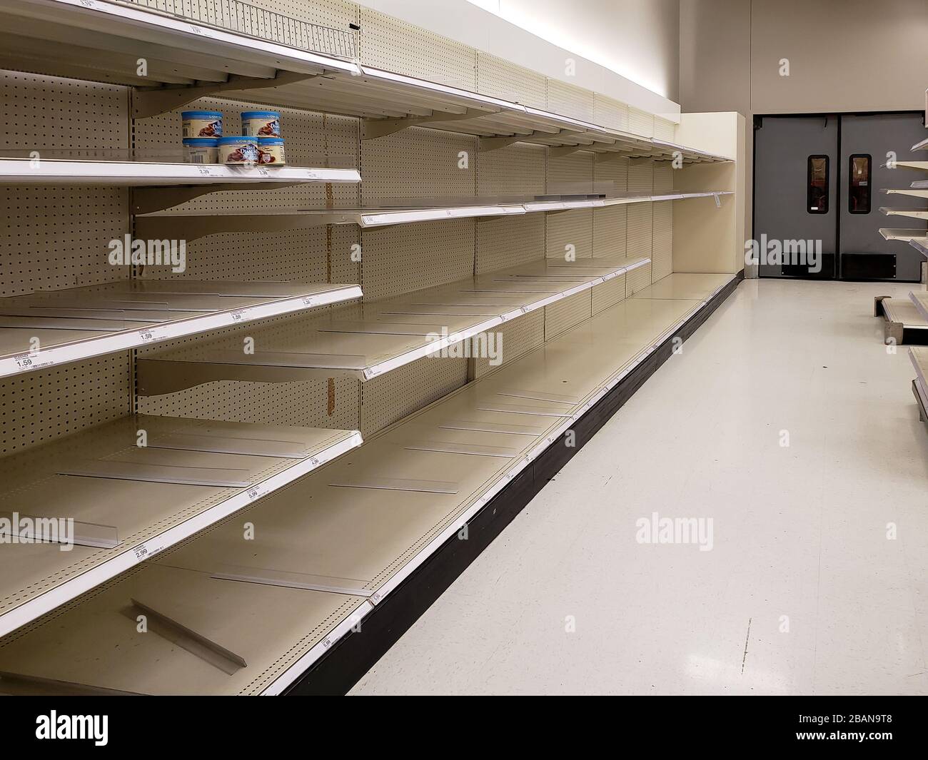 Virtually empty shelves where boxes of facial tissue and paper towels once stood at the back of a market in the San Francisco Bay Area. Oddly a few cans of nuts sit on one shelf out of place. Stock Photo