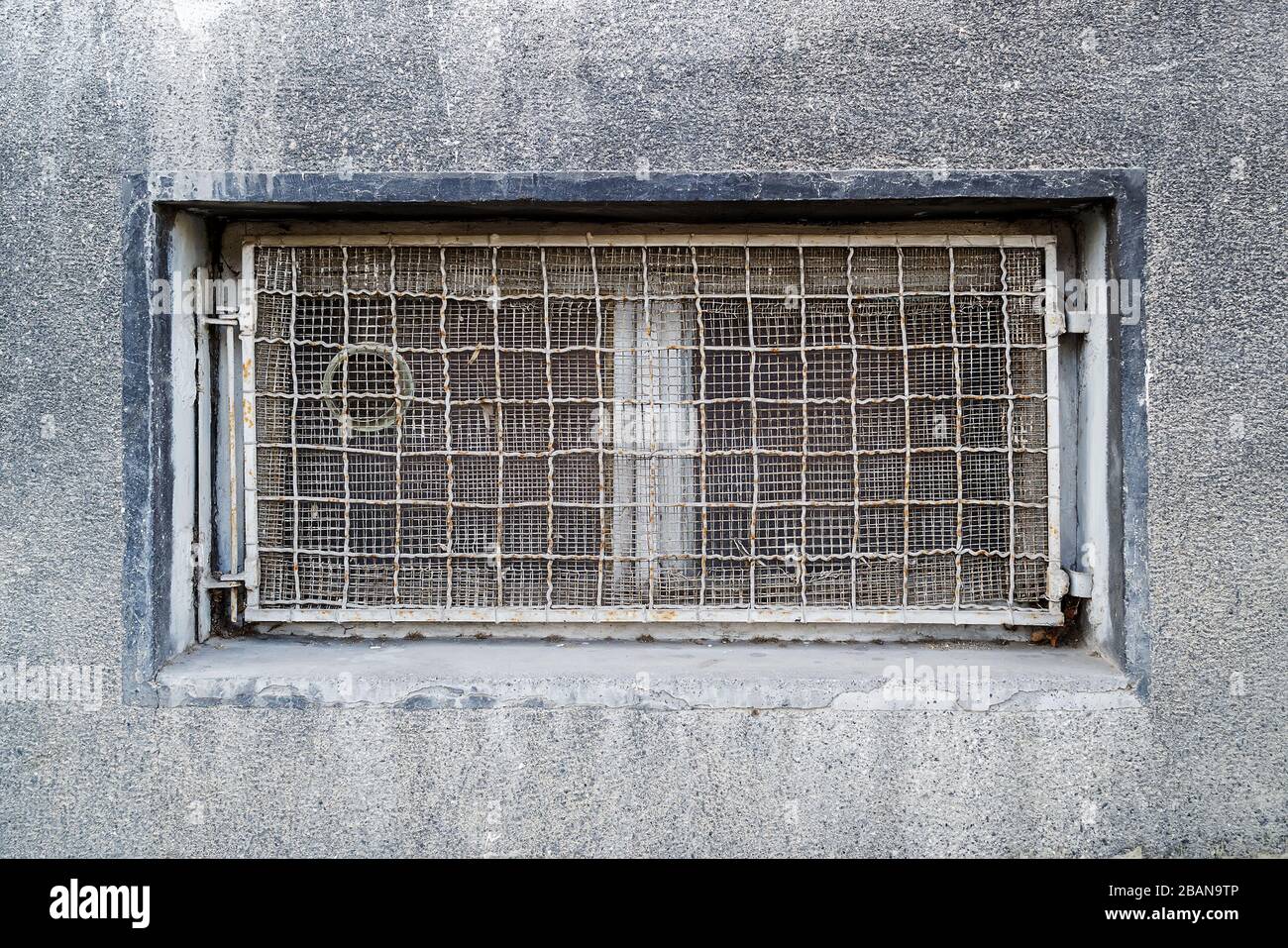 Rectangular basement or cellar window is tightened with wire metal mesh and grille. Technical floor window in the wall of an old gray building. Stock Photo
