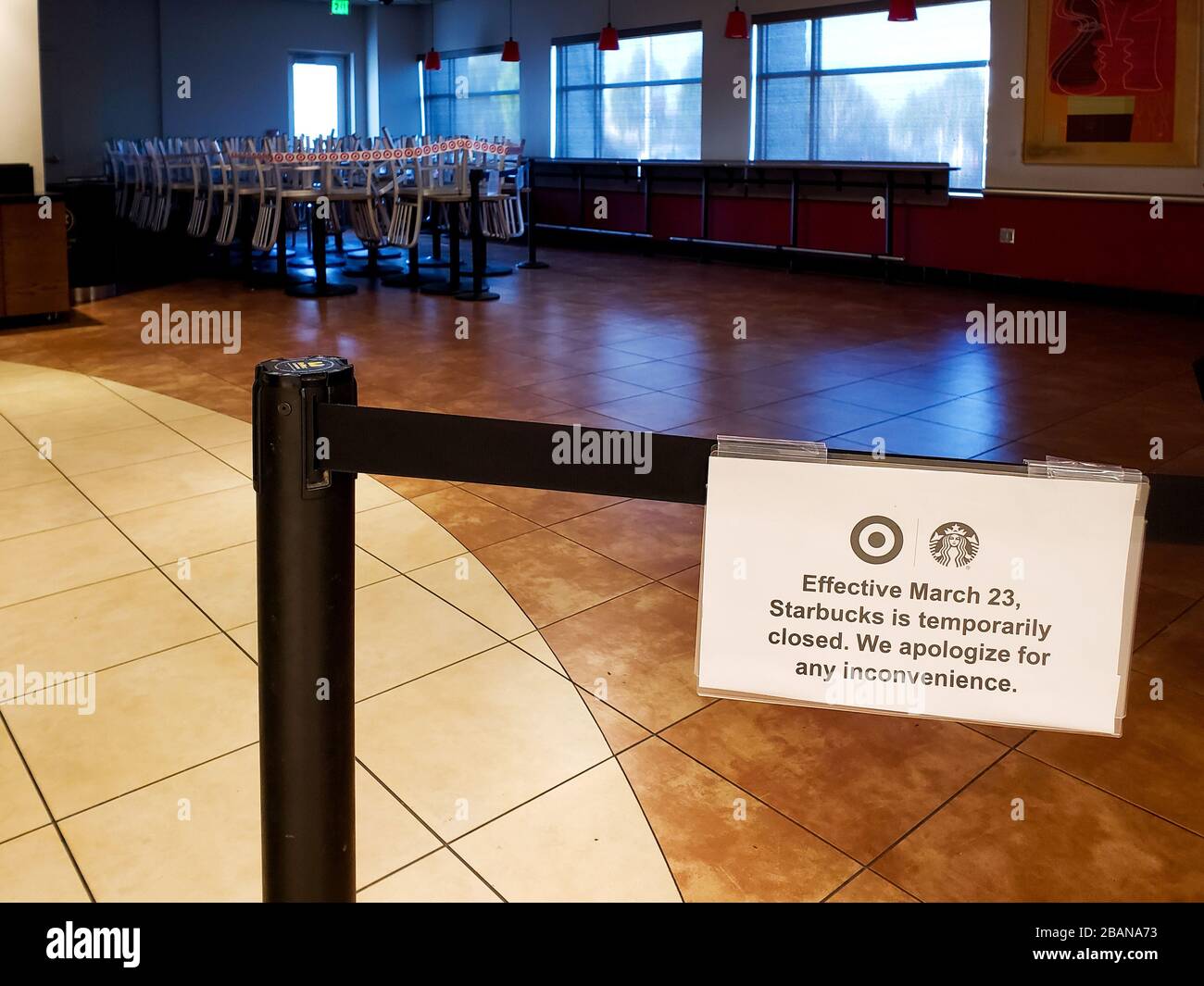 View into a closed Starbuck's cafe with sign reading 'Effective March 23, Starbucks is temproarily closed,' empty with chairs on tables roped off in a dark corner. Stock Photo