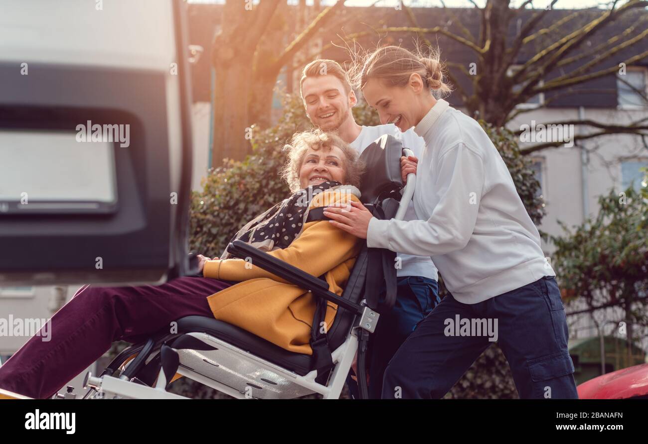 Two helpers picking up disabled senior woman for transport Stock Photo