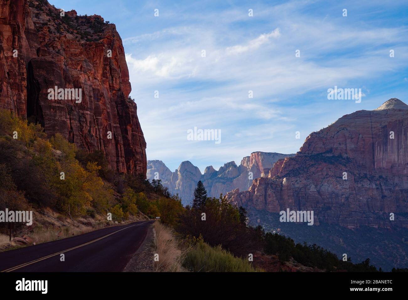 A two lane road hugs the towering red rock cliff on the way up to Zion's tunnel. Stock Photo