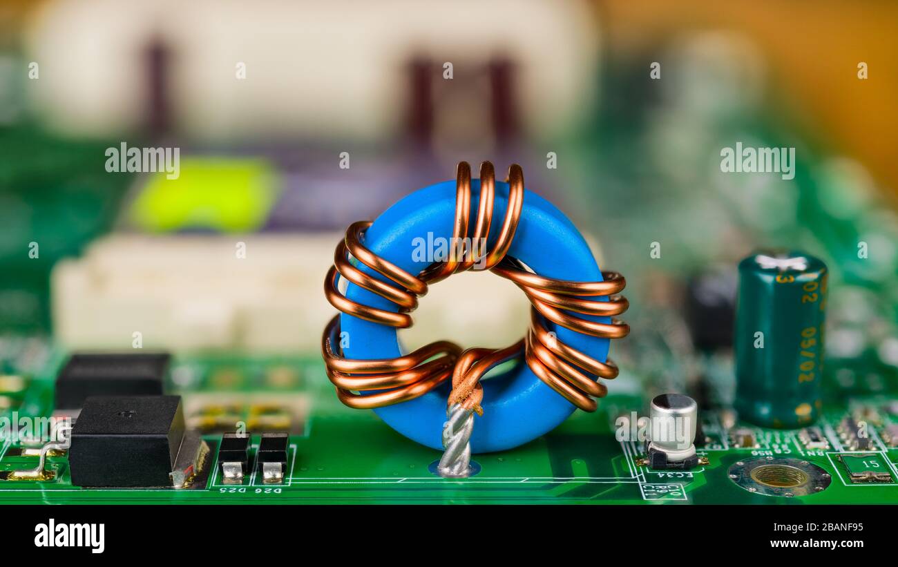 Blue toroidal induction coil on green circuit board. Computer mainboard detail. Electronic components. Ferrite core inductor, capacitor or transistor. Stock Photo