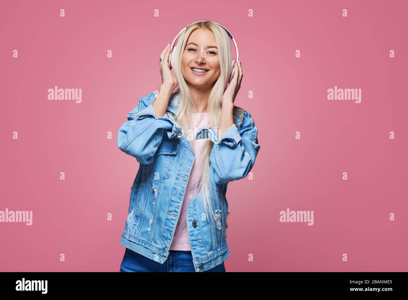 Dentistry and health concept. Pretty young blond woman with broad shining smile wears braces on teeth. Pink background. Listening to music in headphon Stock Photo