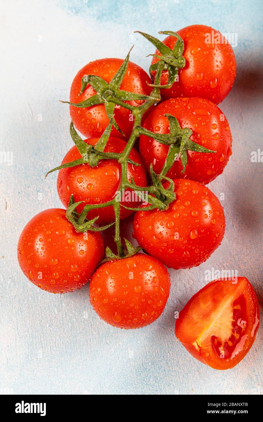 Tomatoes on a branch (vine tomatoes). Tomatoes on the vine and on a blue wood background. Beautiful tomatoes with a beautiful green branch. Stock Photo