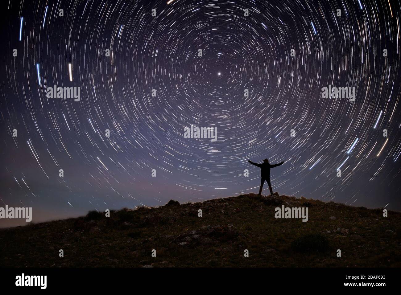 Night landscape with a contour of a man on top of the hill in the mountains against a starry sky with traces of stars rotating around a polar star, in Stock Photo