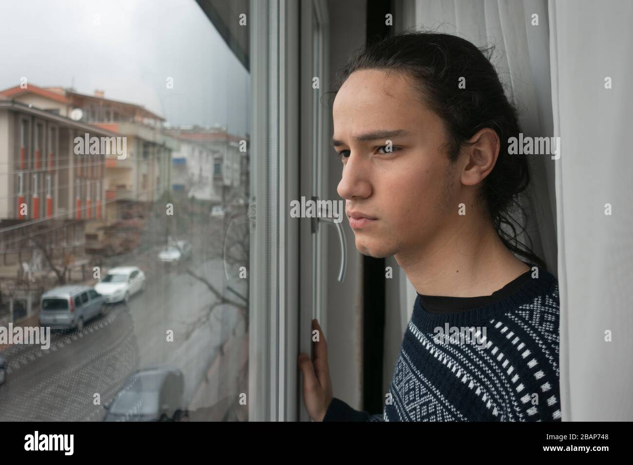 Teen in front of curtain watching the empty street from his window in