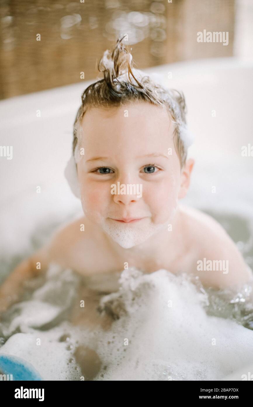 Preschool boy in bathtub with bubbles on face and hair looking at the camera and smiling Stock Photo