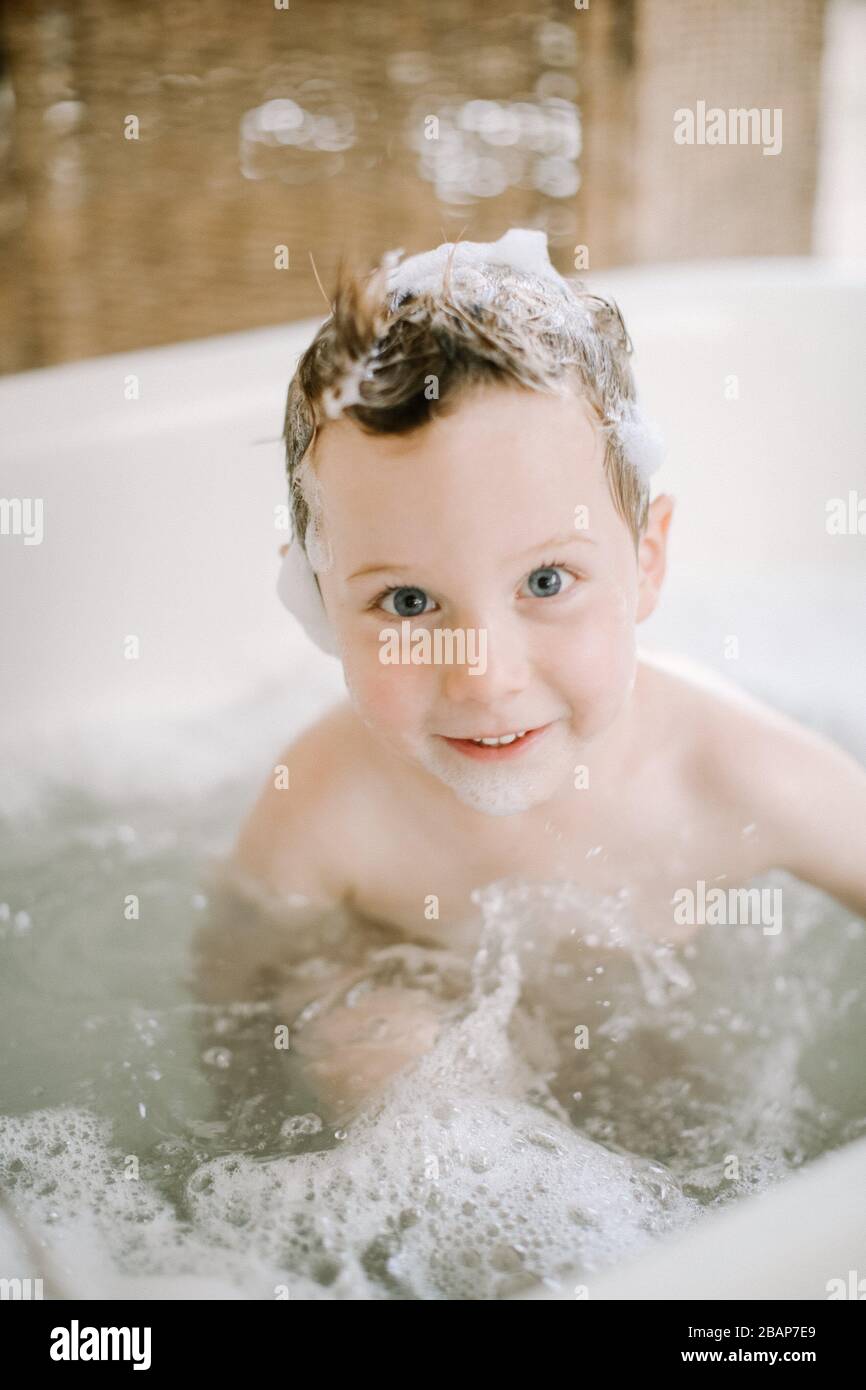 Preschool boy in bathtub with bubbles on face and hair looking at the camera and smiling Stock Photo