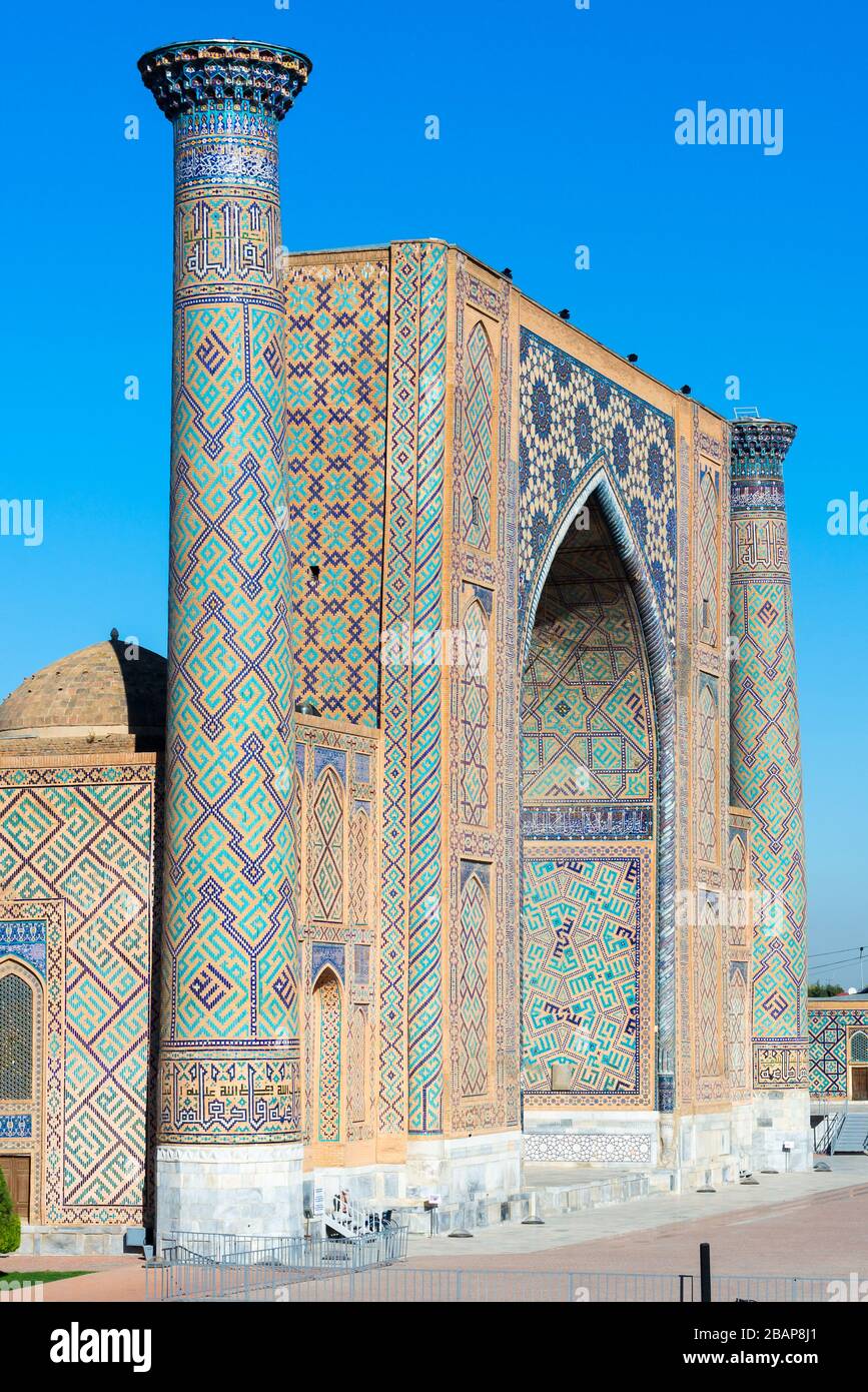 Ulugh Beg Madrasah (Islamic school) and its two minarets with ceramic tiles in Persian style. Vertical photo in the Registan, Samarkand, Uzbekistan. Stock Photo