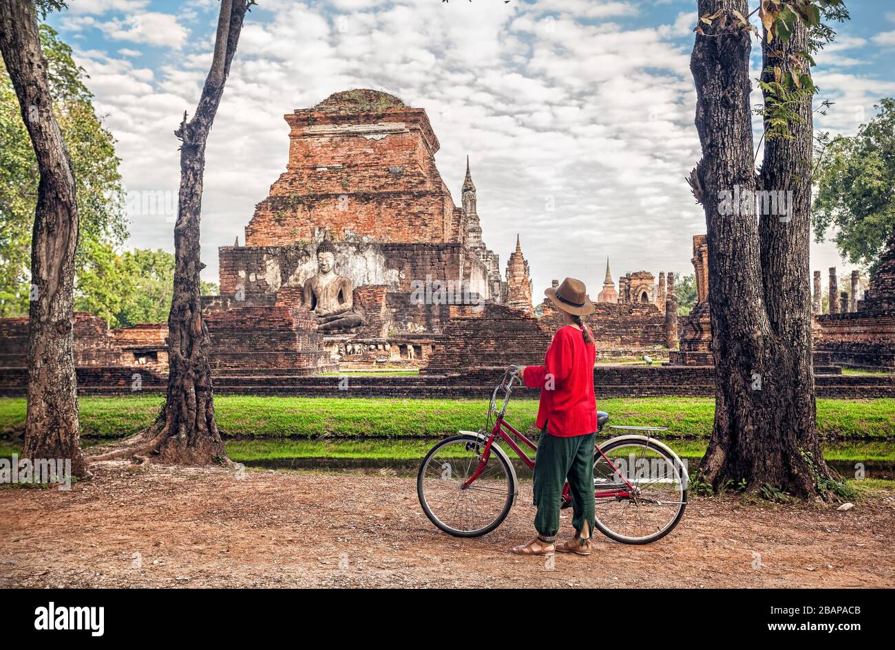 Woman in red shirt riding bicycle looking at old Buddhist temple in Sukhothai historical park, Thailand Stock Photo
