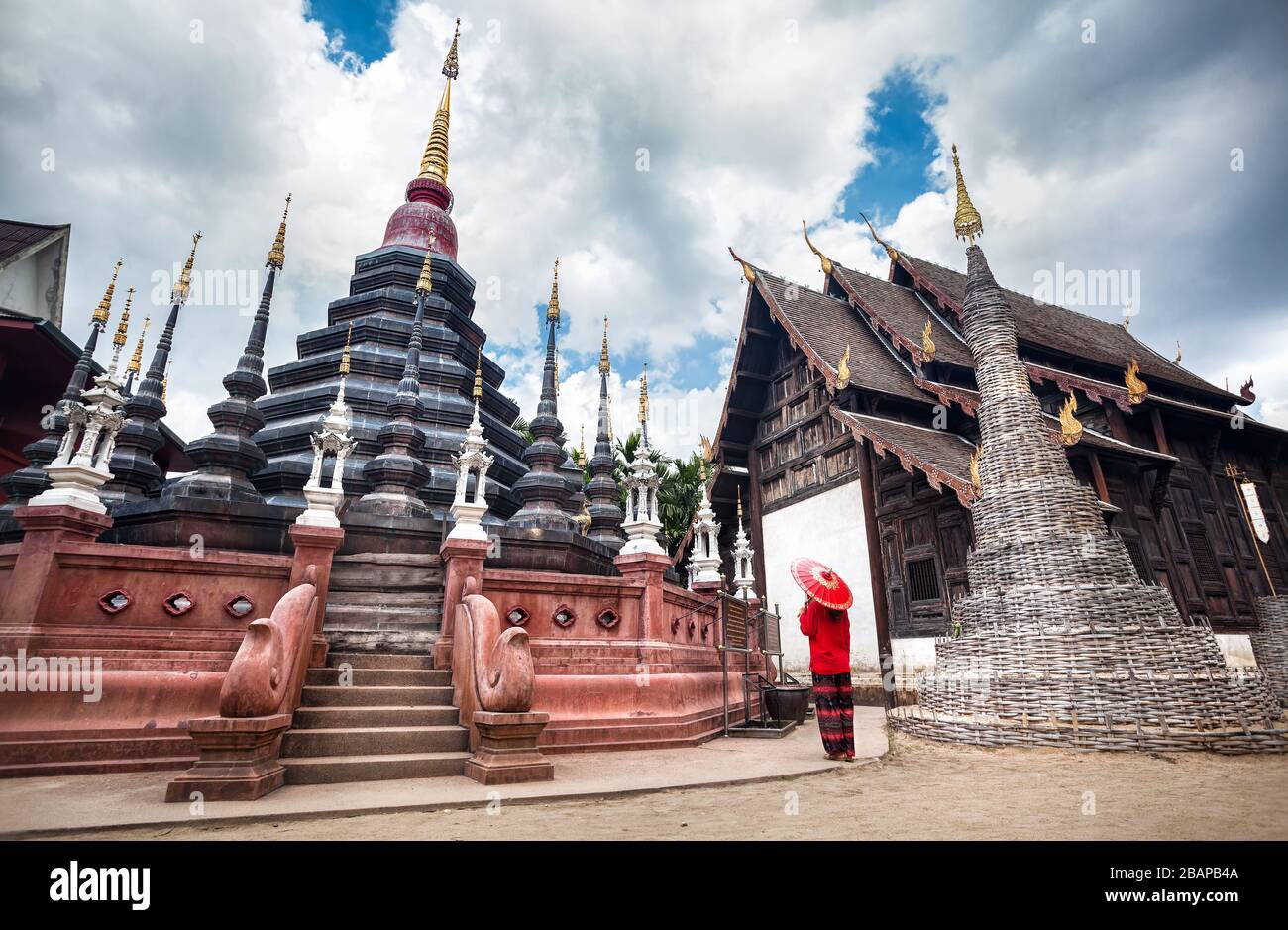 Woman with red traditional Thai umbrella looking at Black temple Wat Phan Tao made from wood in Chiang Mai, Thailand Stock Photo