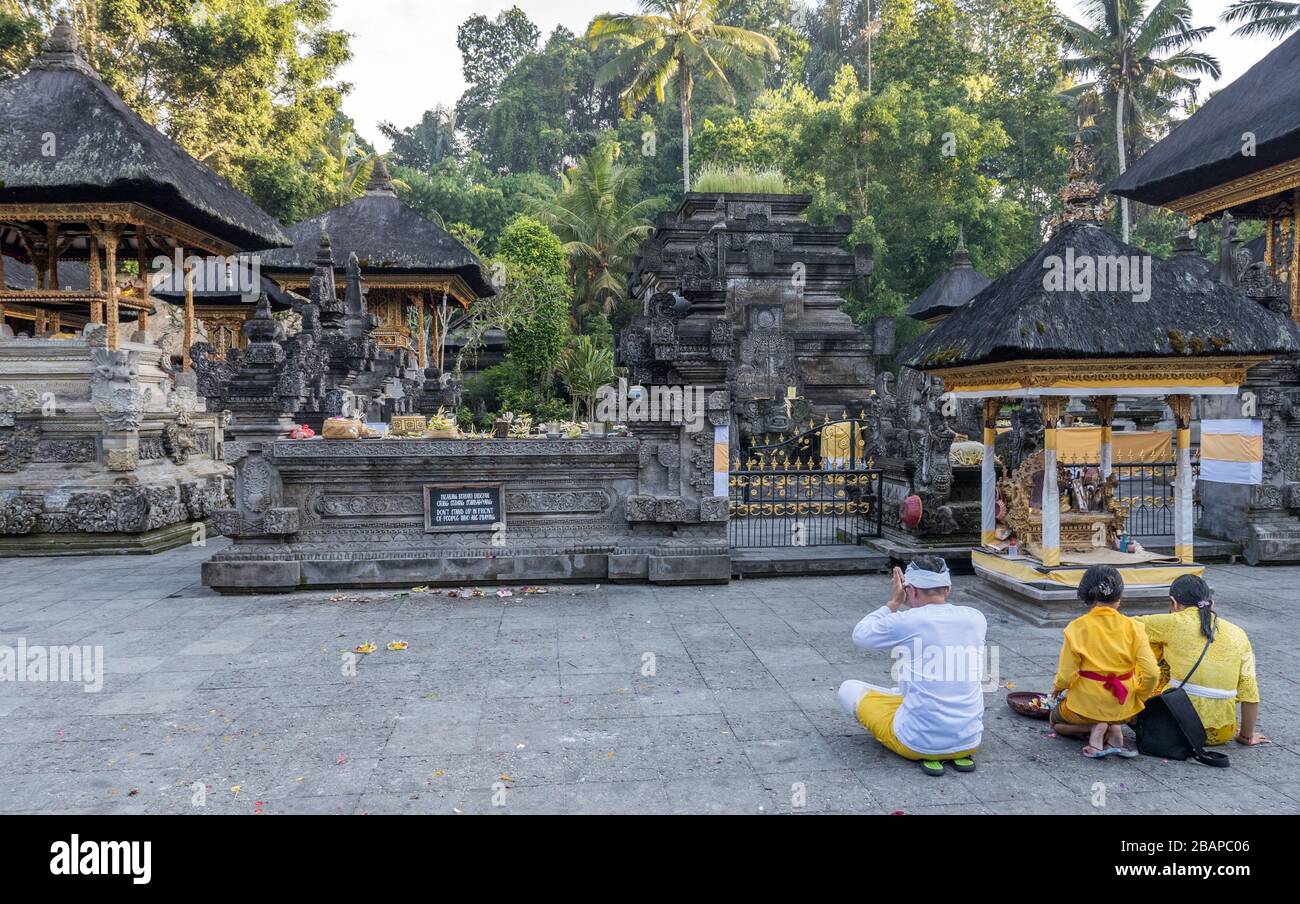 Young Balinese Mother, Father and young daughter in bright colored traditional clothing kneeling in front of temple altar praying to Vishnu. Stock Photo