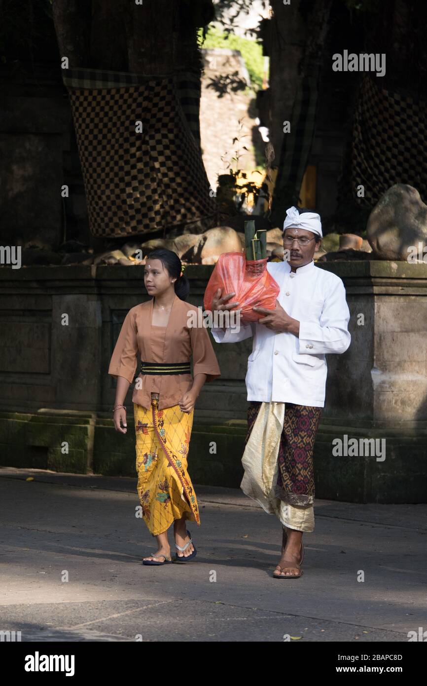 Male and female temple workers dressed in traditional clothing preparing for tourist arrival at Holy Water Temple near Ubud in Bali. Stock Photo