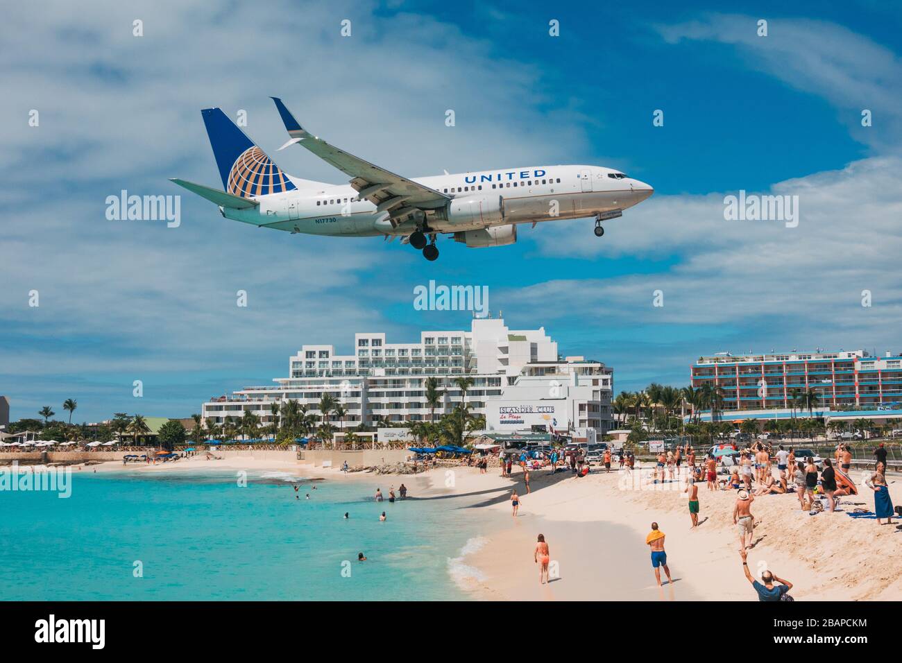 A United Airlines Boeing 737-700 flies over tourists on Maho Beach while landing at St. Maarten Princess Juliana International Airport Stock Photo