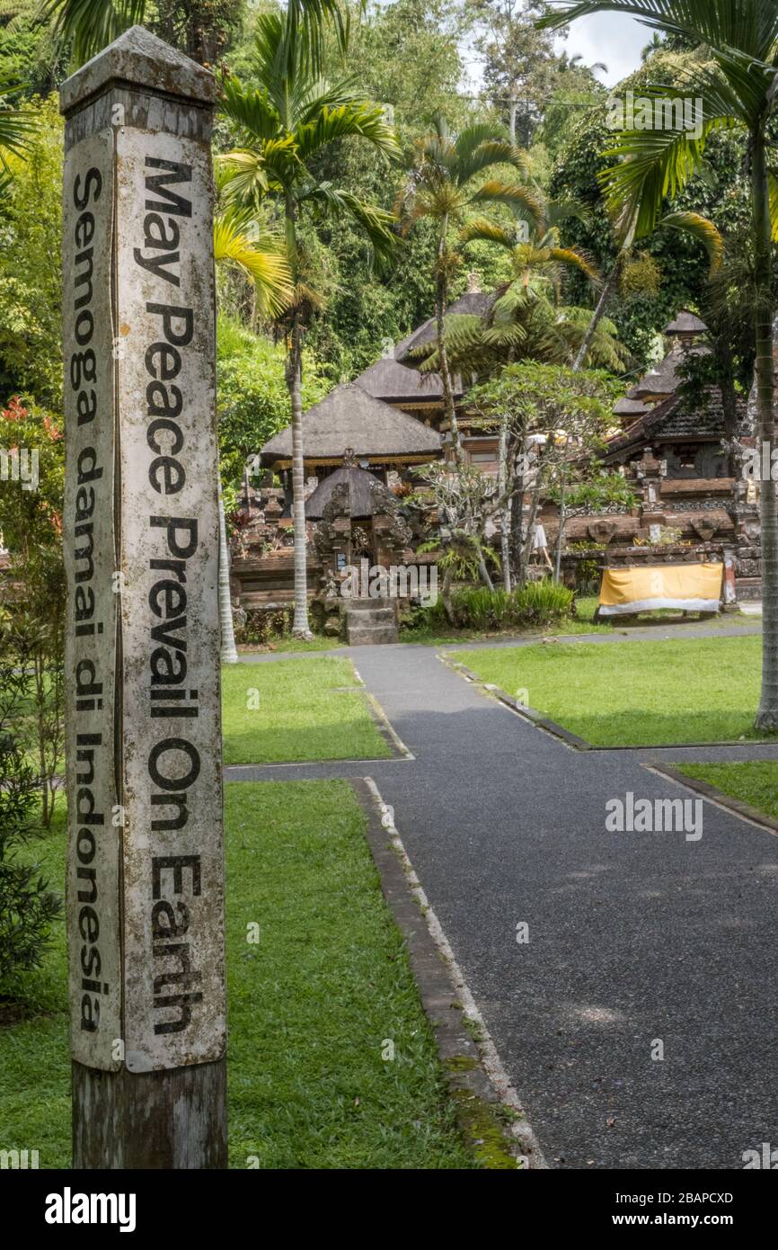 Pura Tirtha Empul or Holy Water Temple entrance sign that says "May Peace Prevail On Earth" carved into stone pillar along sidewalk leading to temple. Stock Photo