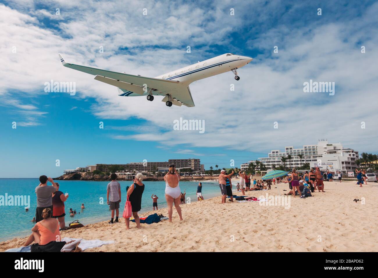 A Gulfstream private jet flies over tourists on Maho Beach, St. Maarten Stock Photo