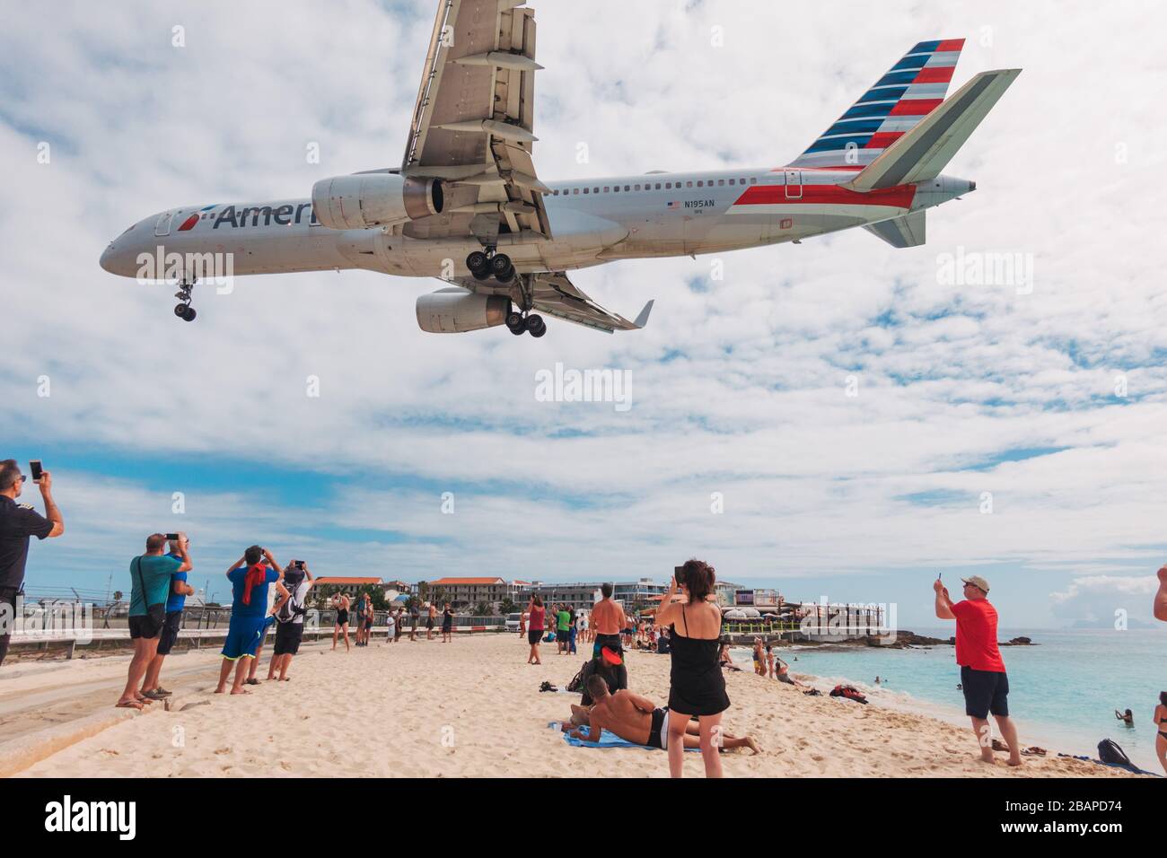 An American Airlines Boeing 757-200 flies low over tourists on Maho Beach, St. Maarten Stock Photo