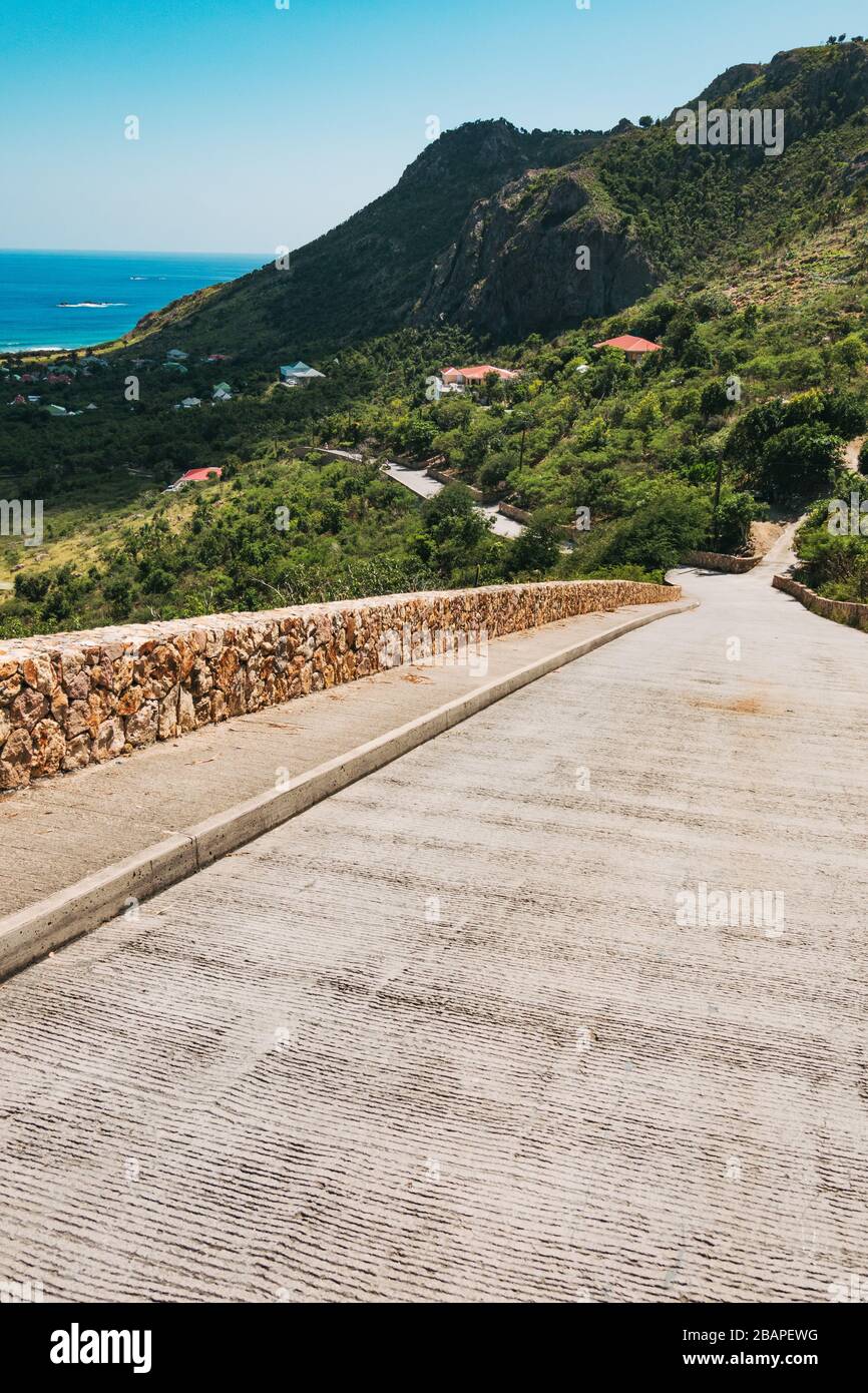 A scenic road down toward the sea with a small stone wall on the island of St Barthélemy, French Caribbean Stock Photo