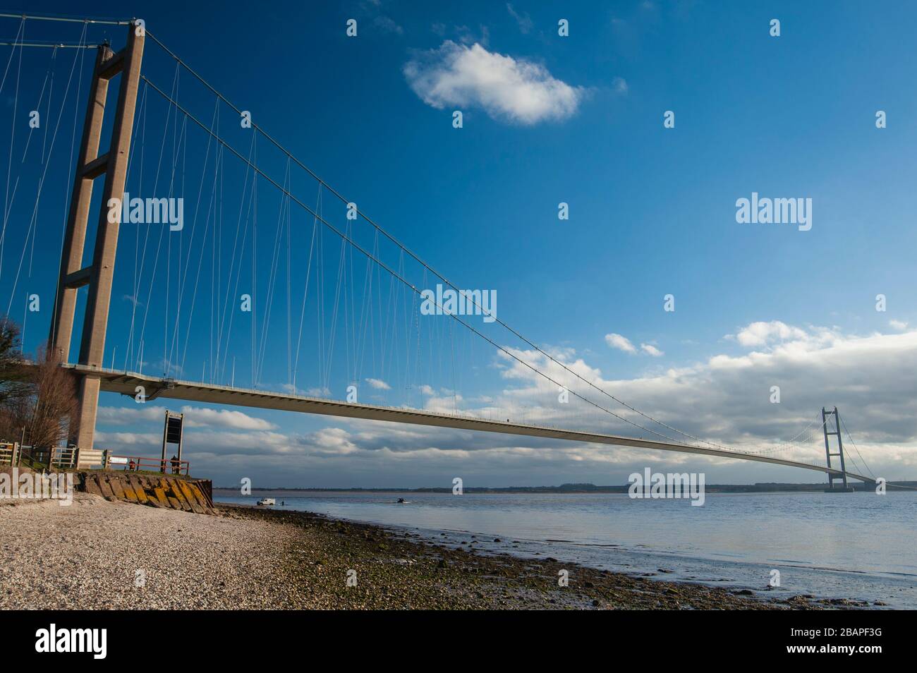 Large suspension bridge spanning a wide river estuary on a clear day with blue sky and clouds Stock Photo