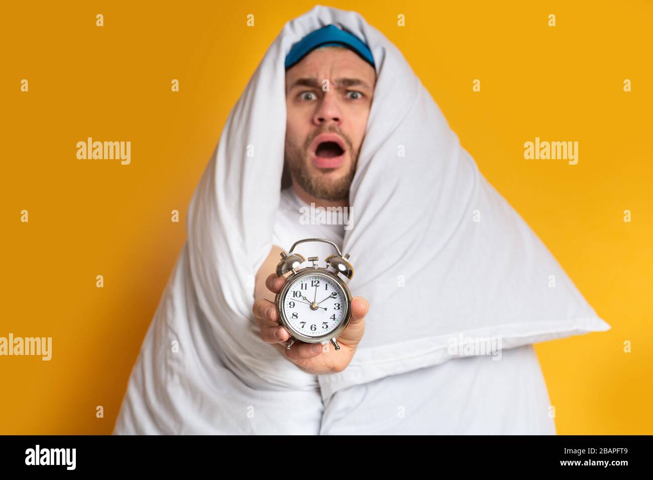 Emotional guy in blanket holding an alarm clock Stock Photo