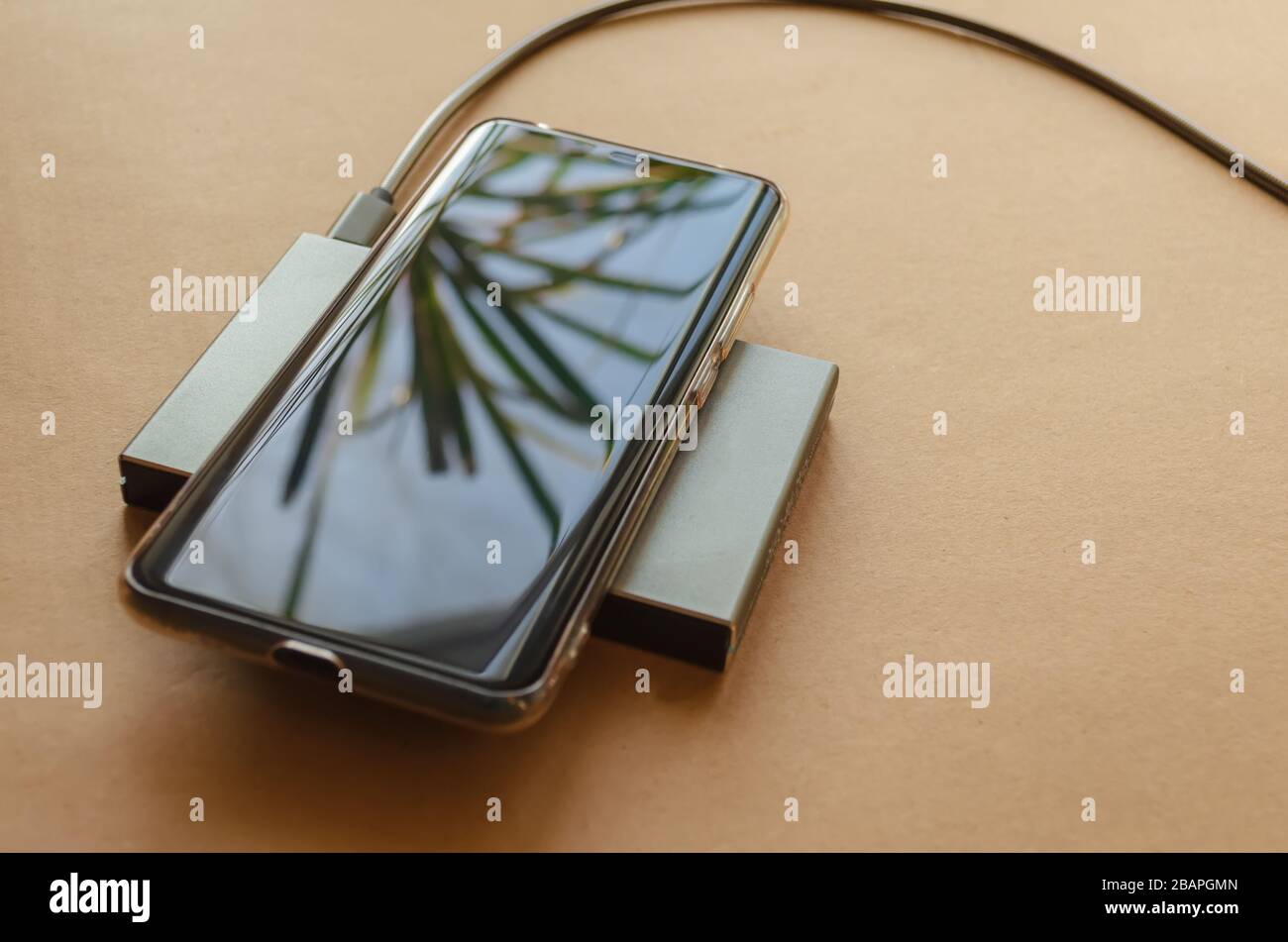 The phone is charging from a rectangular induction charger. Wireless charger. Copy space Stock Photo
