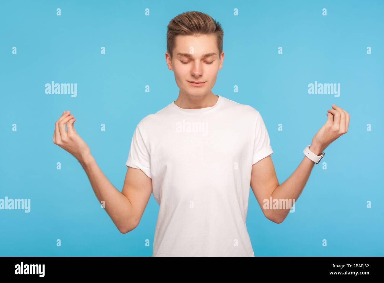 Relaxation, mind harmony. Portrait of man in casual white t-shirt holding arms in mudra gesture and meditating with peaceful expression, practicing yo Stock Photo