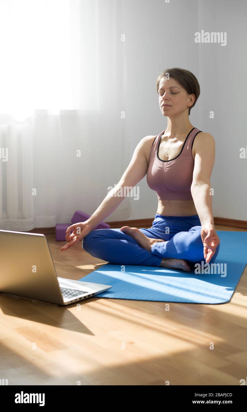 A woman meditates yoga online through a laptop. Stock Photo