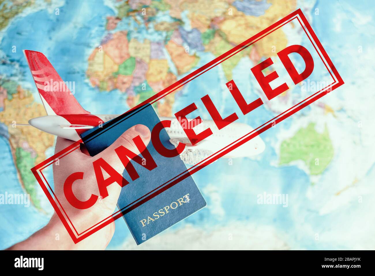 Crisis in tourism industry and stop travel due to coronavirus covid-19. Toy plane in hand and passport against world map and inscription cancelled Stock Photo