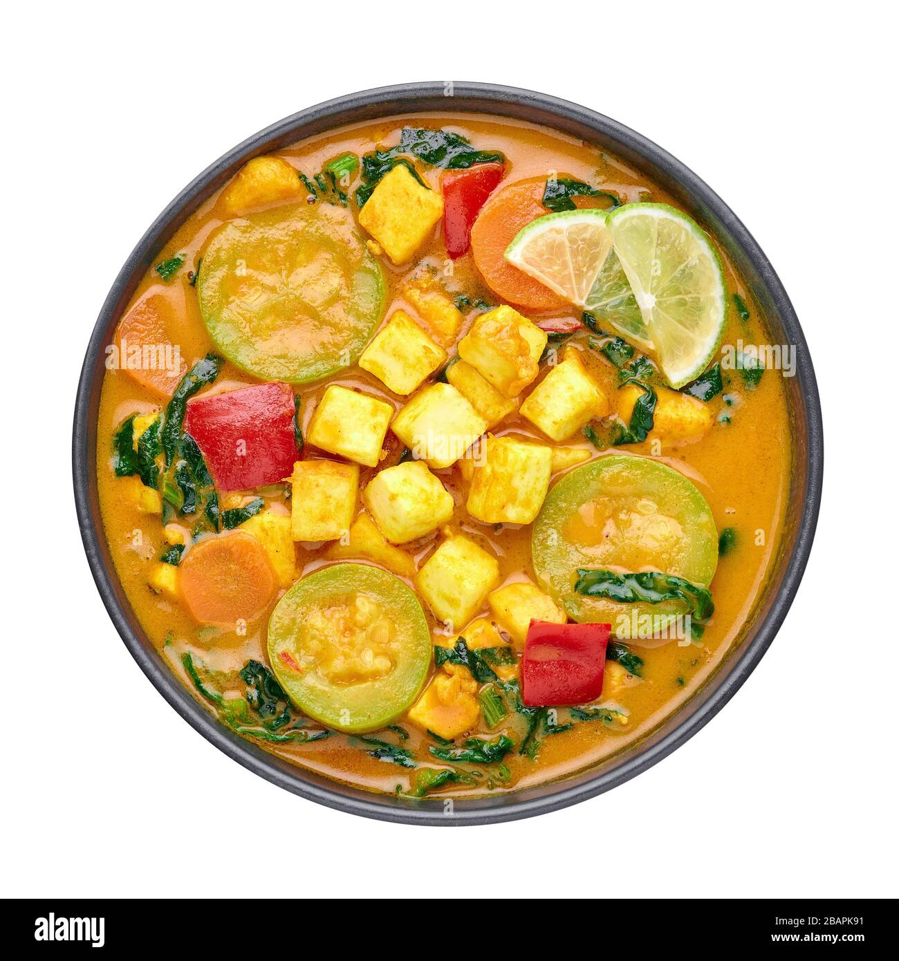 A Yellow Veg Thai Curry with Tofu and vegetables isolated on white background. Vegetarian Thai Curry with tofu, zucchini, bell pepper, spinach, carrot Stock Photo