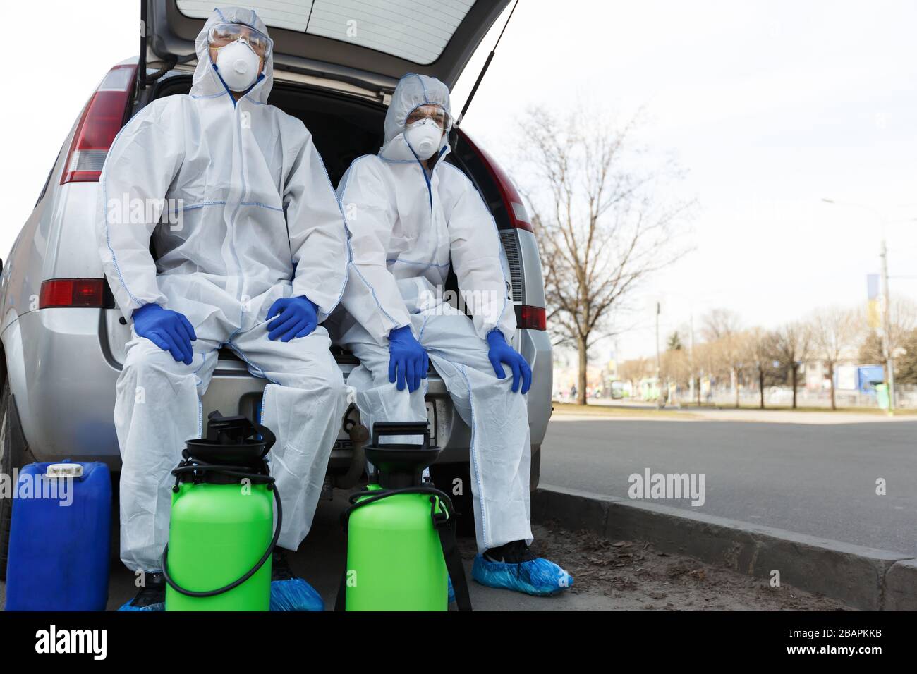Men in biohazard suits sitting in car with disinfection chemicals Stock