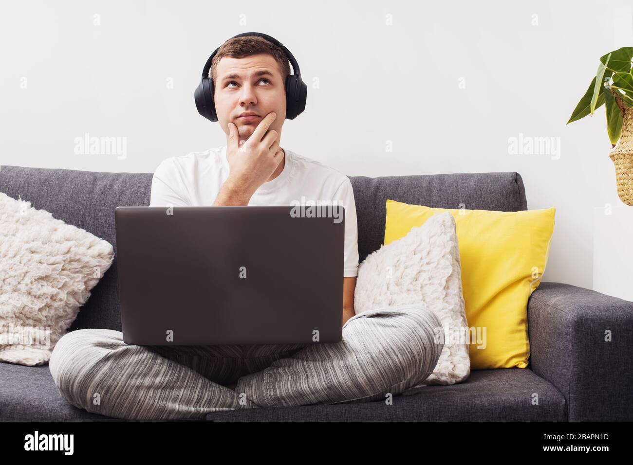 Doubtful young man looking up while working on laptop Stock Photo