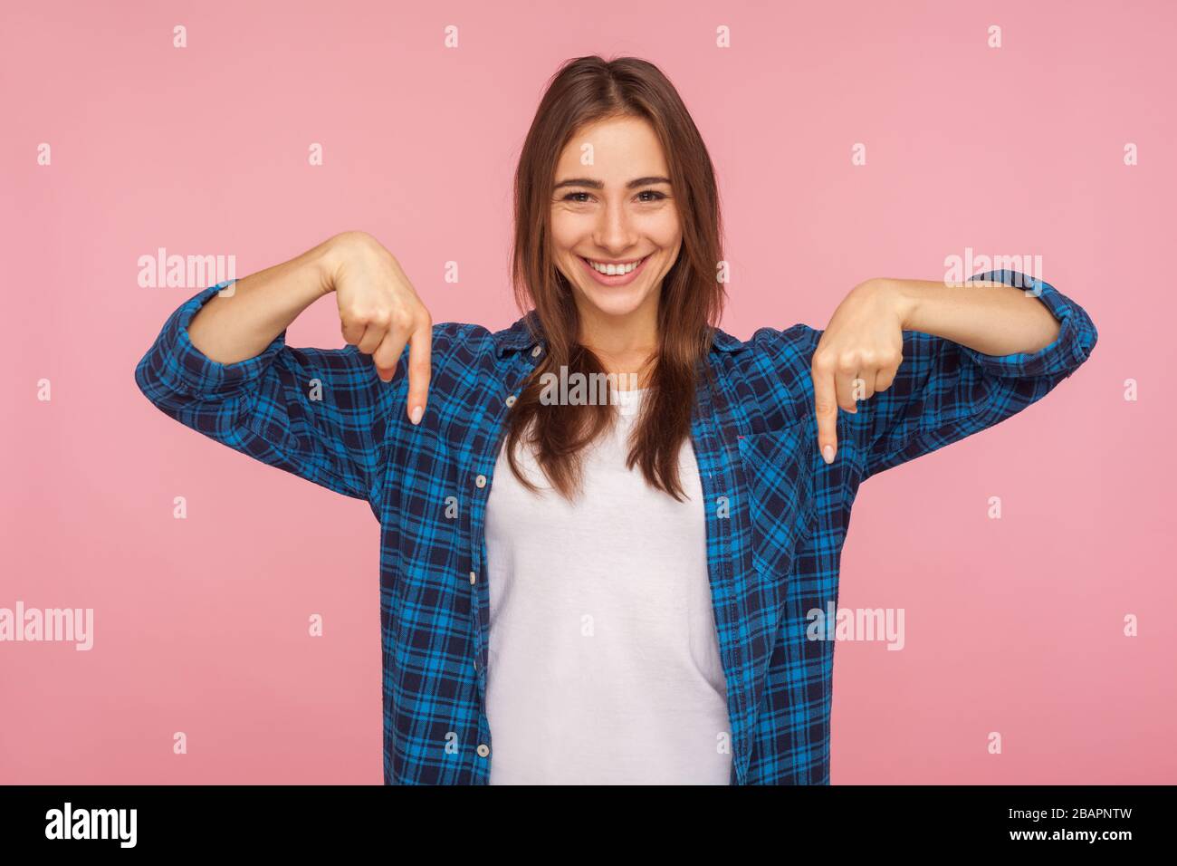 Look down, choose option below! Portrait of charming brunette girl in checkered shirt pointing down at place for advertisement, commercial content. in Stock Photo