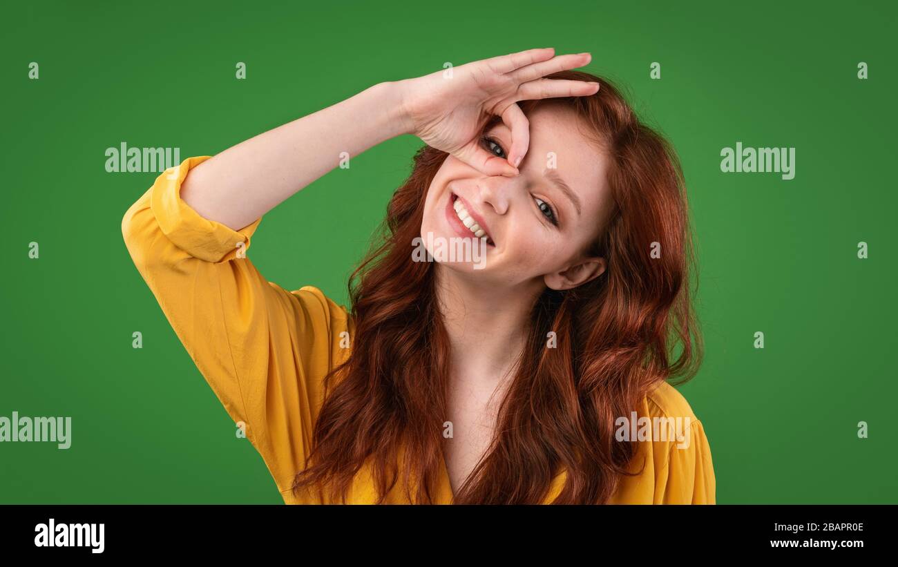 Girl Gesturing Okay Holding Hand Near Eye, Green Background, Panorama Stock Photo