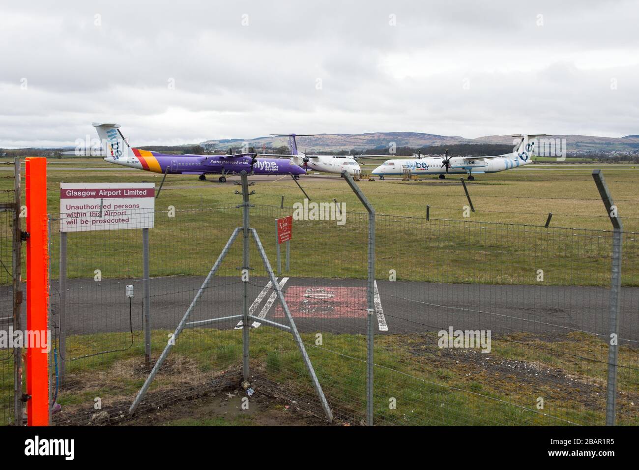 Glasgow, UK. 27 March 2020. Pictured: Grounded Flybe De Havilland Canada Dash 8 Q400 Aircraft seen parked up on the tarmac by the Emergency Rendezvous point at Glasgow Airport.  The Coronavirus Pandemic has been responsible for the UK shutdown aviation bringing Glasgow Airport to look more like a ghost town. Credit: Colin Fisher/Alamy Live News. Stock Photo