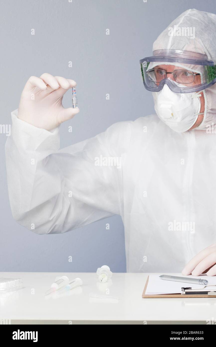 Doctor with surgical mask and protective clothing looking at a vaccine in his hand Stock Photo