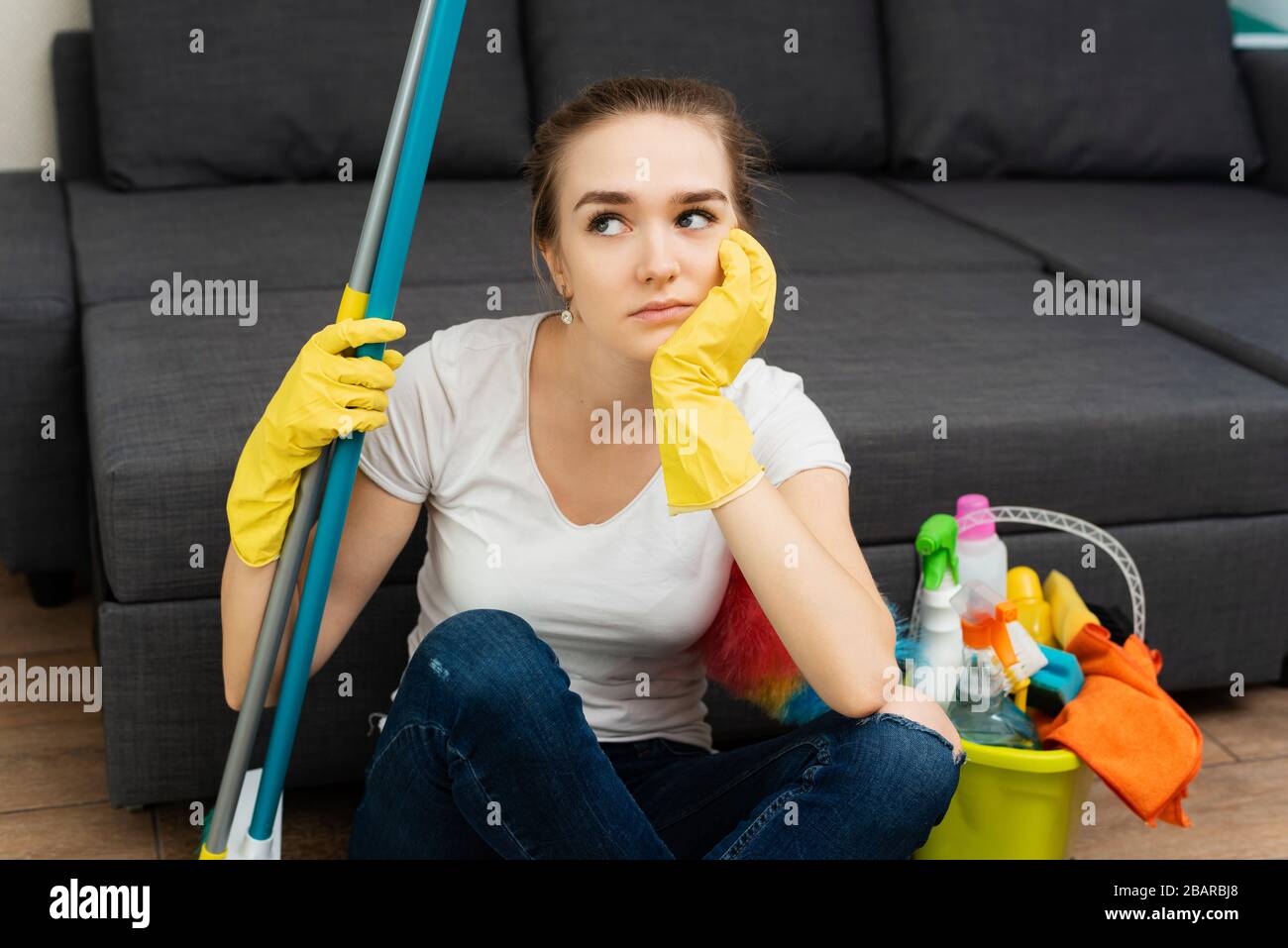 A beautiful woman in rubber gloves next to a coat and cleaning products gets angry at a lot of household chores. Problems of distribution of household duties. Stock Photo