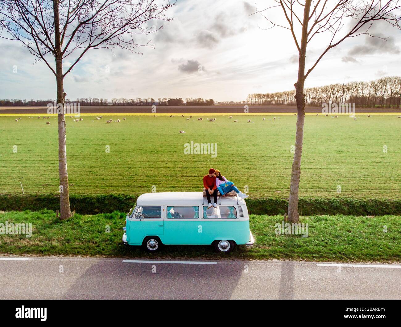 Noordoostpolder Netherlands April 2019, Classic Green and white VW Camper Van parked with couple watching the Sunrise over the meadow during Spring Stock Photo