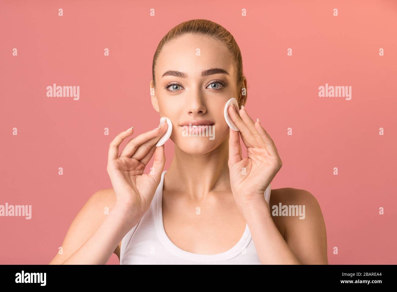 Girl using cotton pads looking at camera on pink background Stock Photo