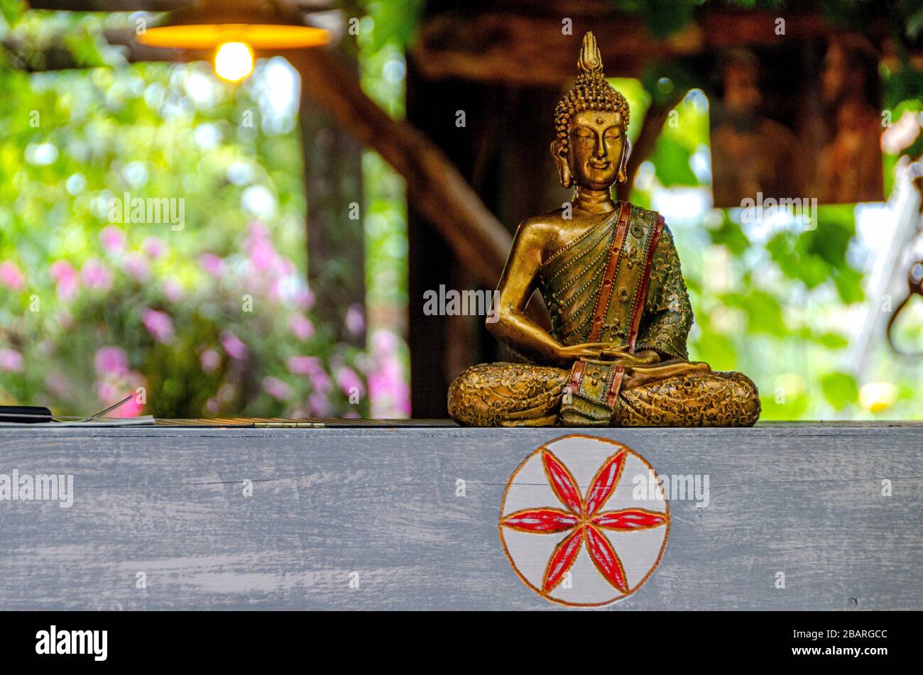 A bronze Buddha statue in the lotus position standing on a wooden, stylish beam in a designer interior Stock Photo