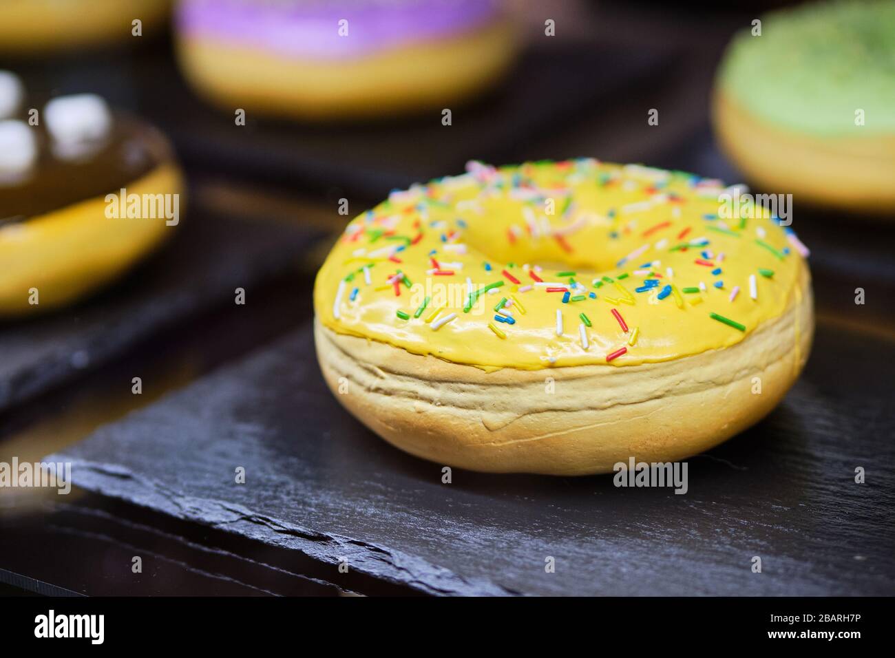 A delicious donut lies on a stone board in a restaurant window. Close up. Stock Photo