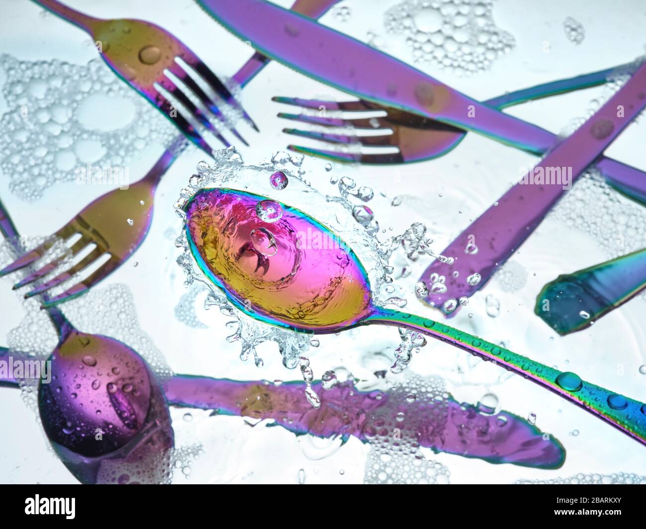 Washing colorful silverware in kitchen sink with splashes and bubbles Stock Photo