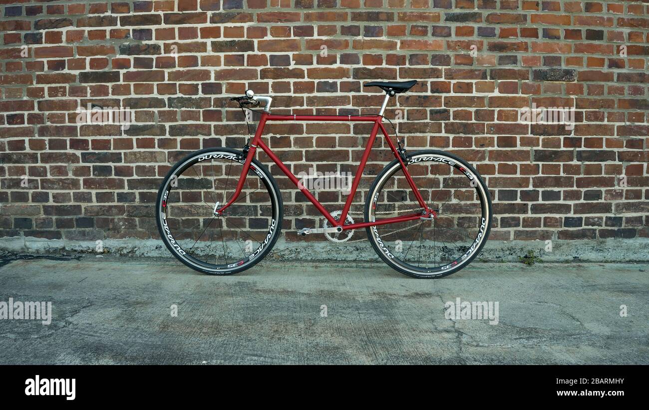 Retro styled red Singlespeed fixed gear bike leaning isolated on a brick wall Stock Photo