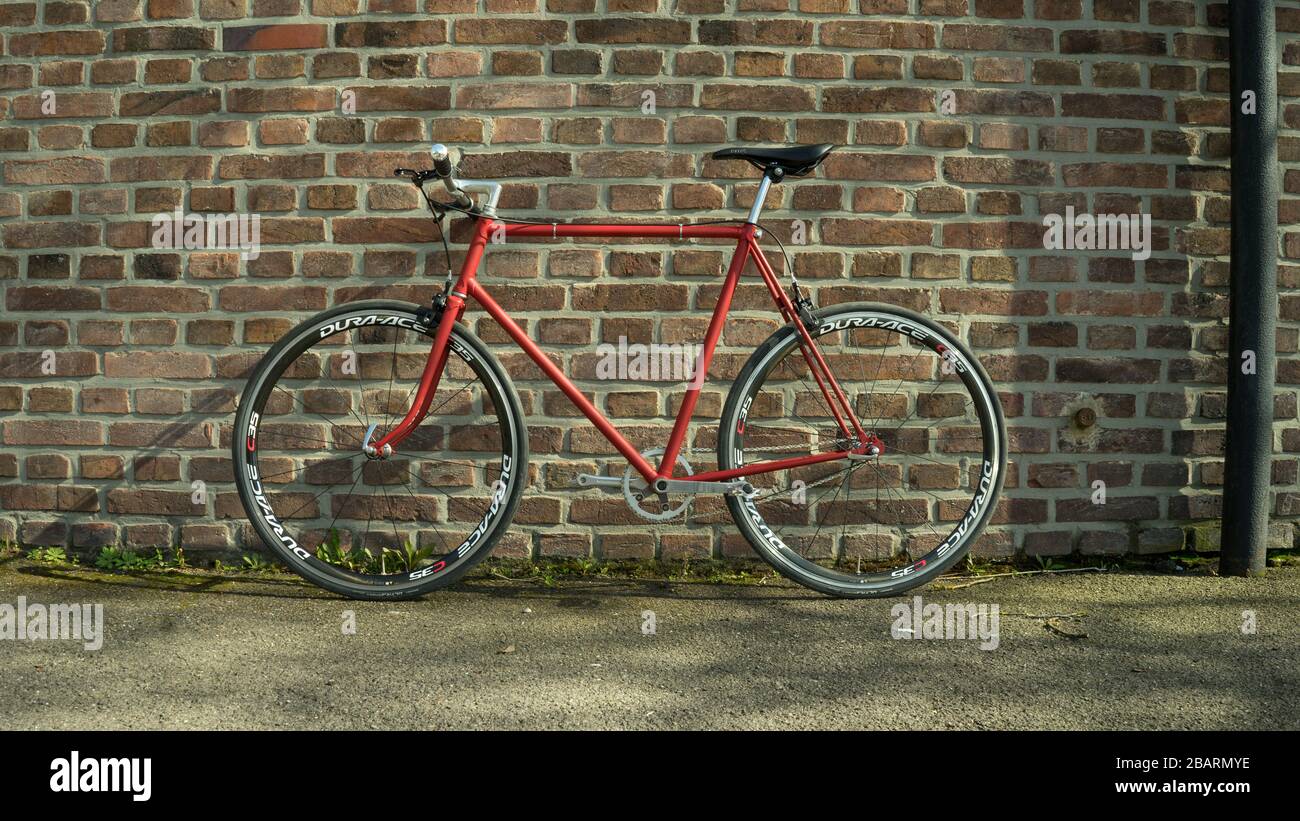 Retro styled red Singlespeed fixed gear bike leaning isolated on a brick wall Stock Photo