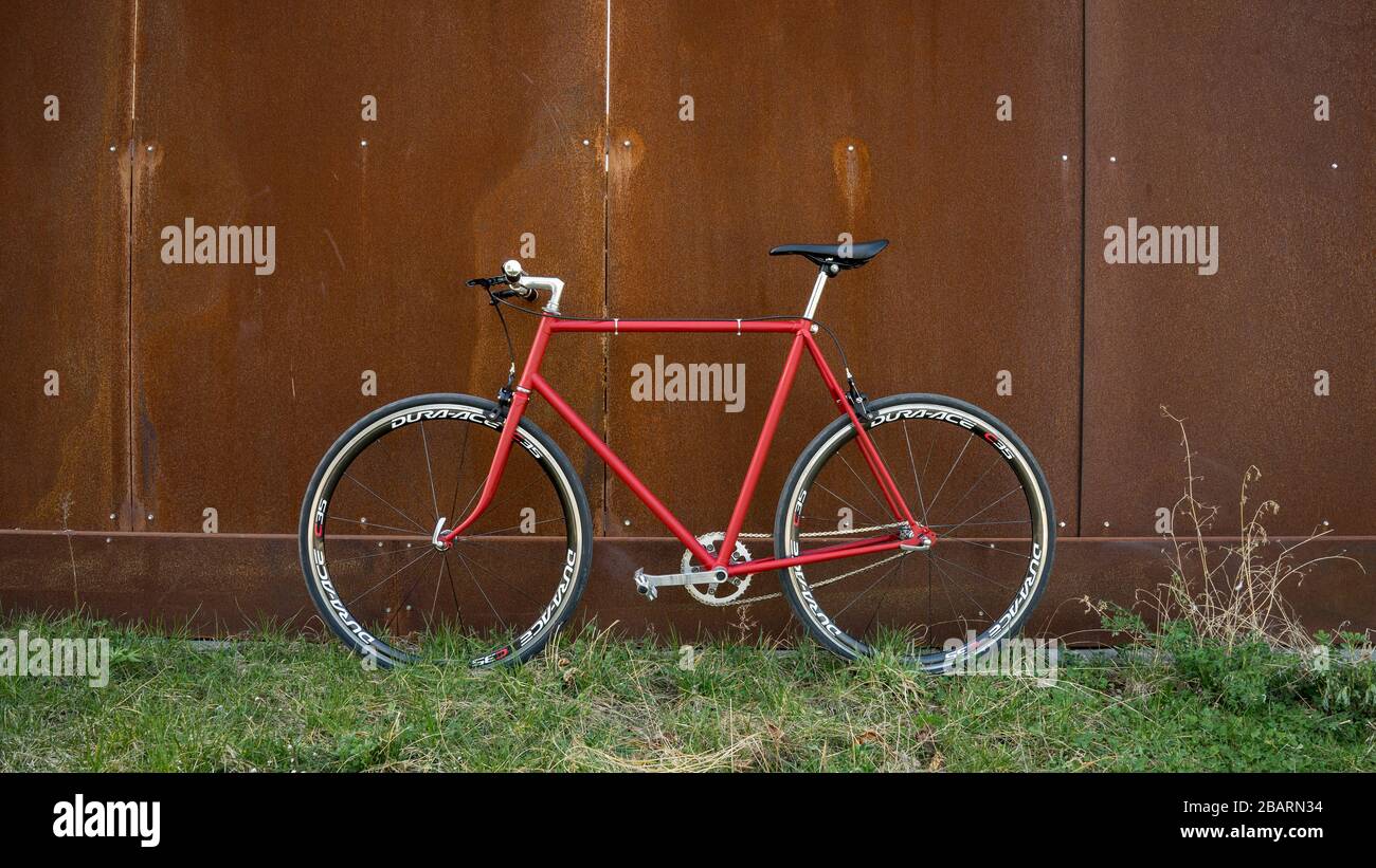 Retro styled red Singlespeed fixed gear bike leaning isolated on a metal wall Stock Photo